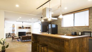A modern kitchen with a wooden island, bar stools, and pendant lighting. - Coton (Kanonji)