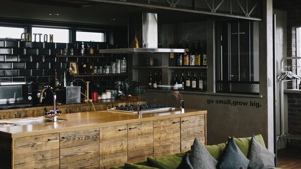 A modern kitchen with wooden cabinetry, a stainless steel range hood, and a bar area with bottles. - Coton (Kanonji)