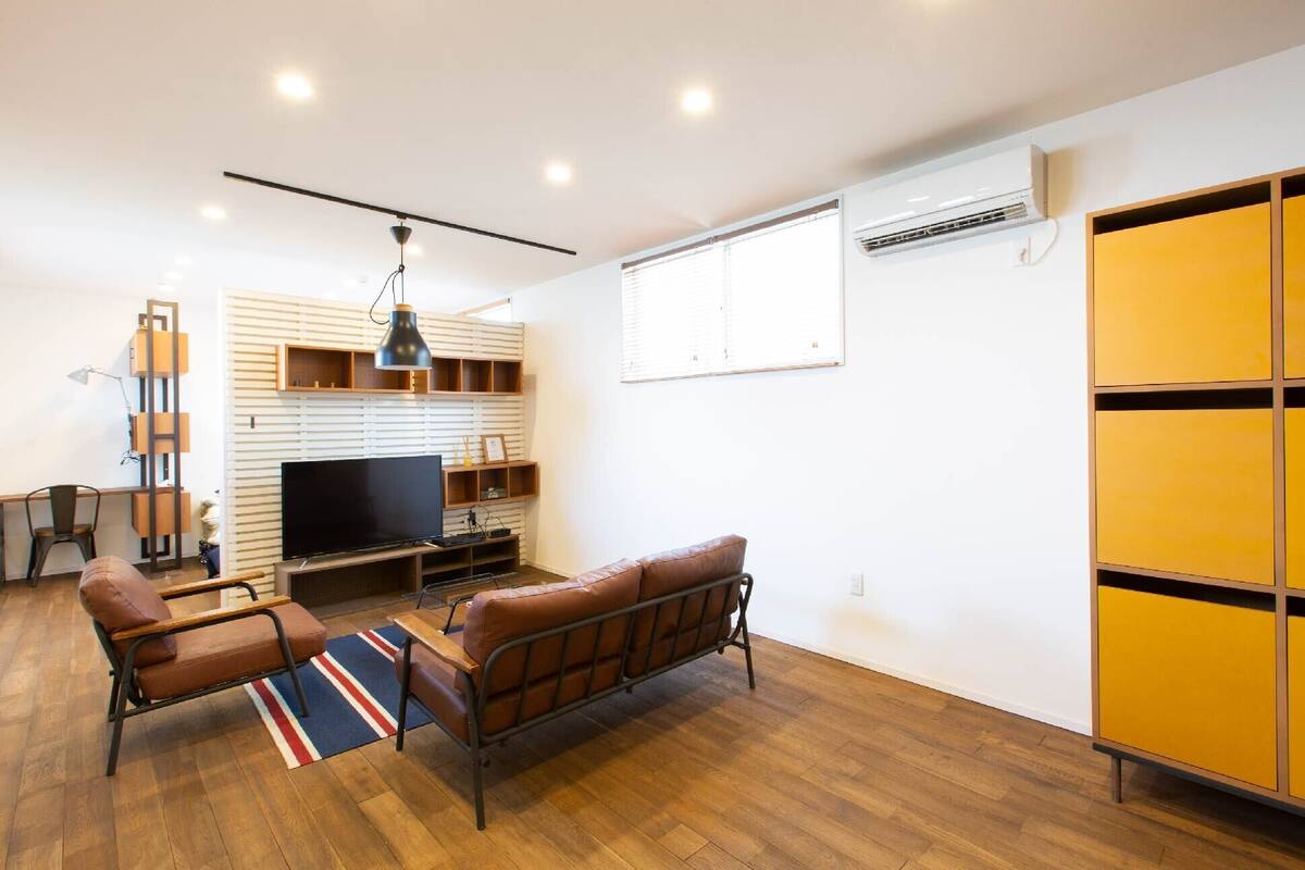 A modern living room with a flat-screen TV, leather sofa, wooden floor, and a yellow cabinet.