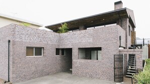 A modern brick house with a flat roof, a small garden, and a metal gate. - Coton (Kanonji)