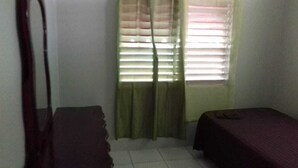 Ein kleines Zimmer mit einem Bett, einem Stuhl und einem Fenster mit Jalousien.