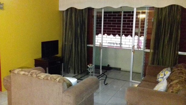Ein Wohnzimmer mit einer Couch, einem Fernseher und einer Schiebetür, die auf einen Balkon führt.