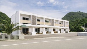 A modern hotel with a white facade, multiple balconies, and a view of a lush green mountain.