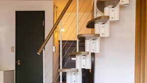 A modern staircase with a wooden handrail and white steps, leading to a dark door.