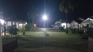 A nighttime view of a residential area with houses, a well-lit street, and a gated entrance. - JEYs Place (Nilaveli)