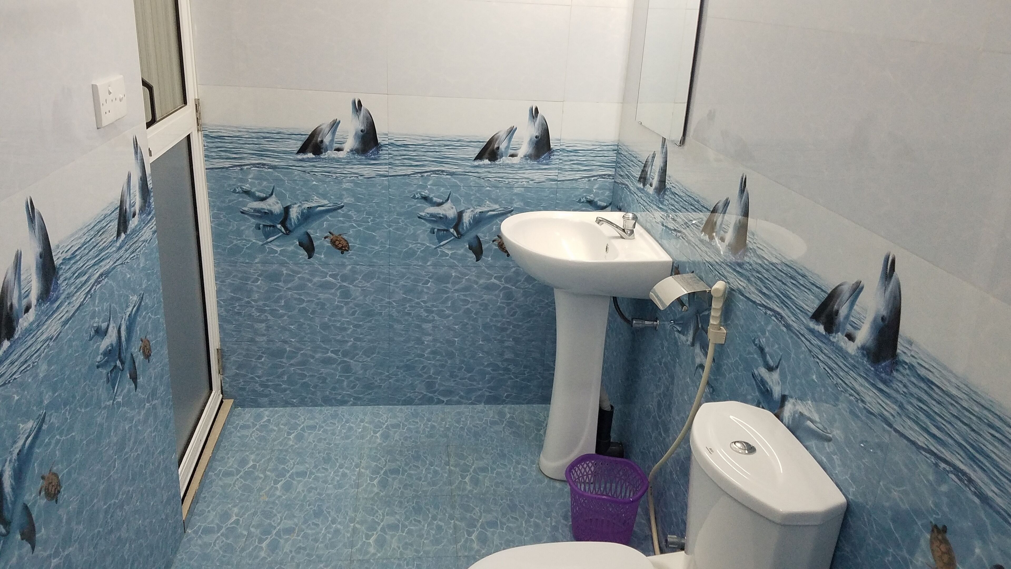 A bathroom with a blue tiled floor and walls, decorated with dolphin murals.