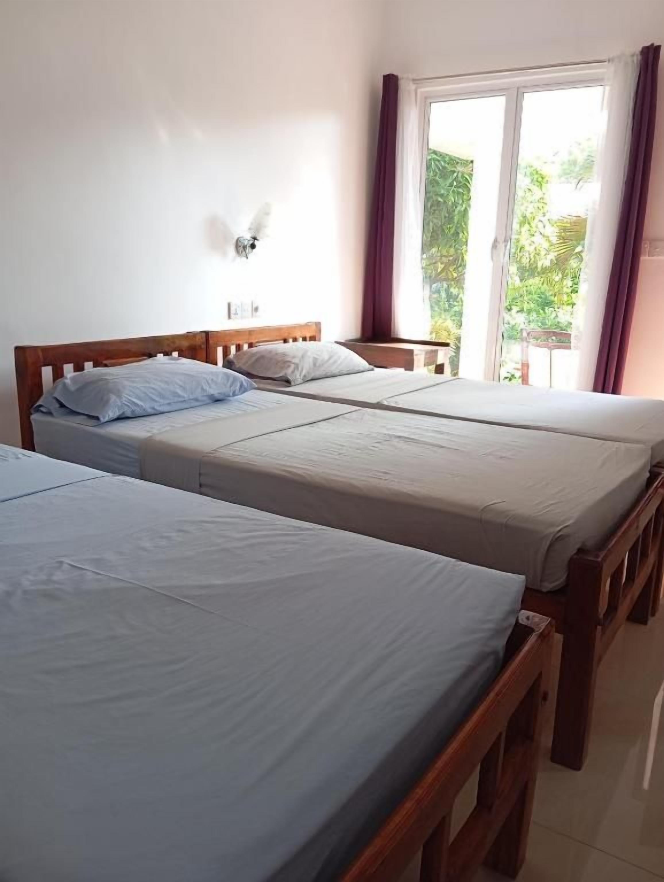 Habitación de hotel con dos camas individuales, una ventana con cortinas y vistas a zonas verdes.