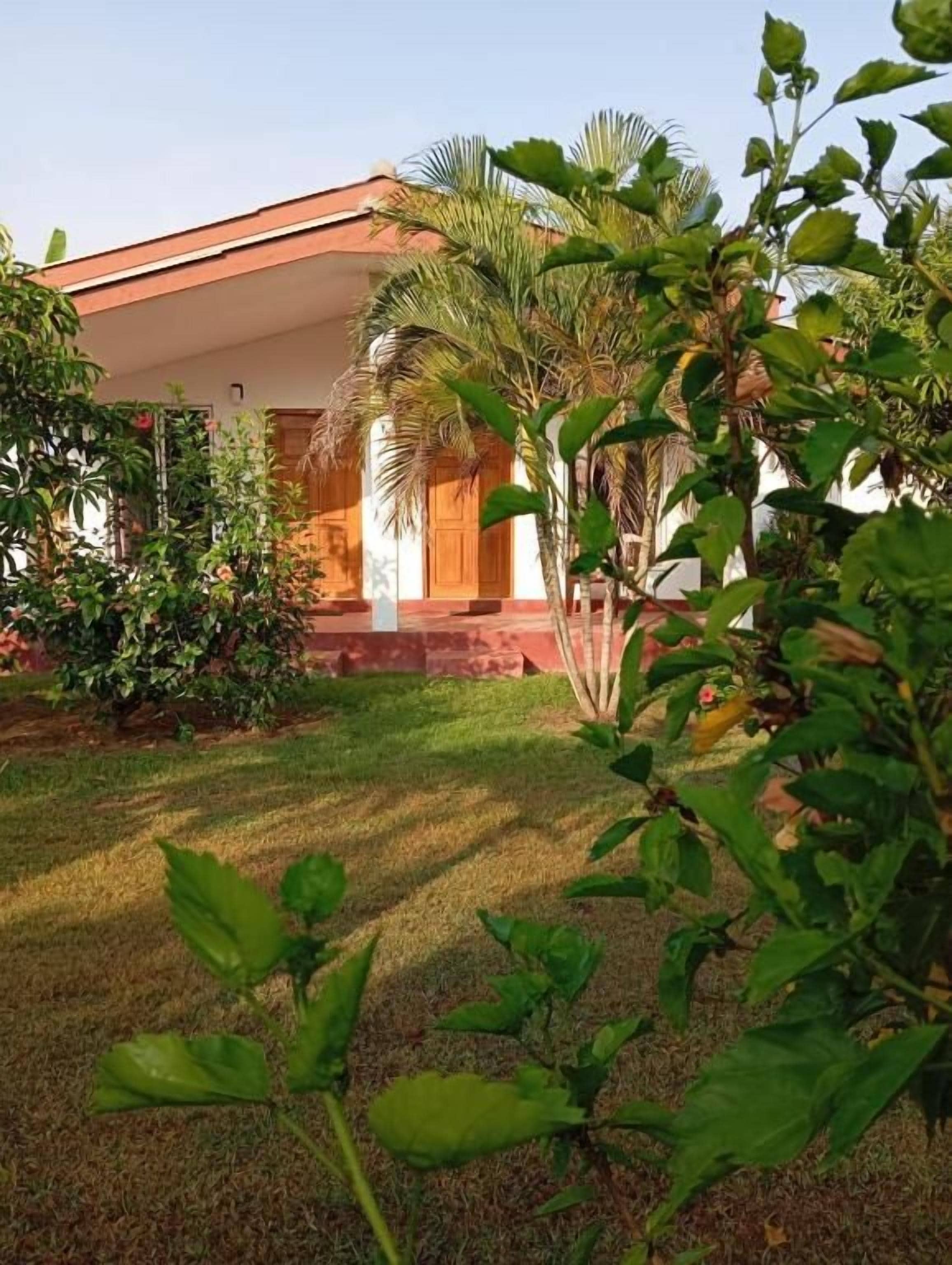 Un bâtiment doté d’un toit rouge, entouré d’un jardin bien entretenu où poussent différentes espèces de plantes et un palmier.