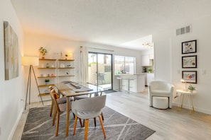 Relax in a stylish living space with a dining area, seating nook, and kitchen, offering a view of palm trees through a sliding glass door.