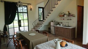 A dining area with a table, chairs, a chandelier, a staircase, and a kitchen area with shelves and a refrigerator. - Moshang Caoxun (Changbin)