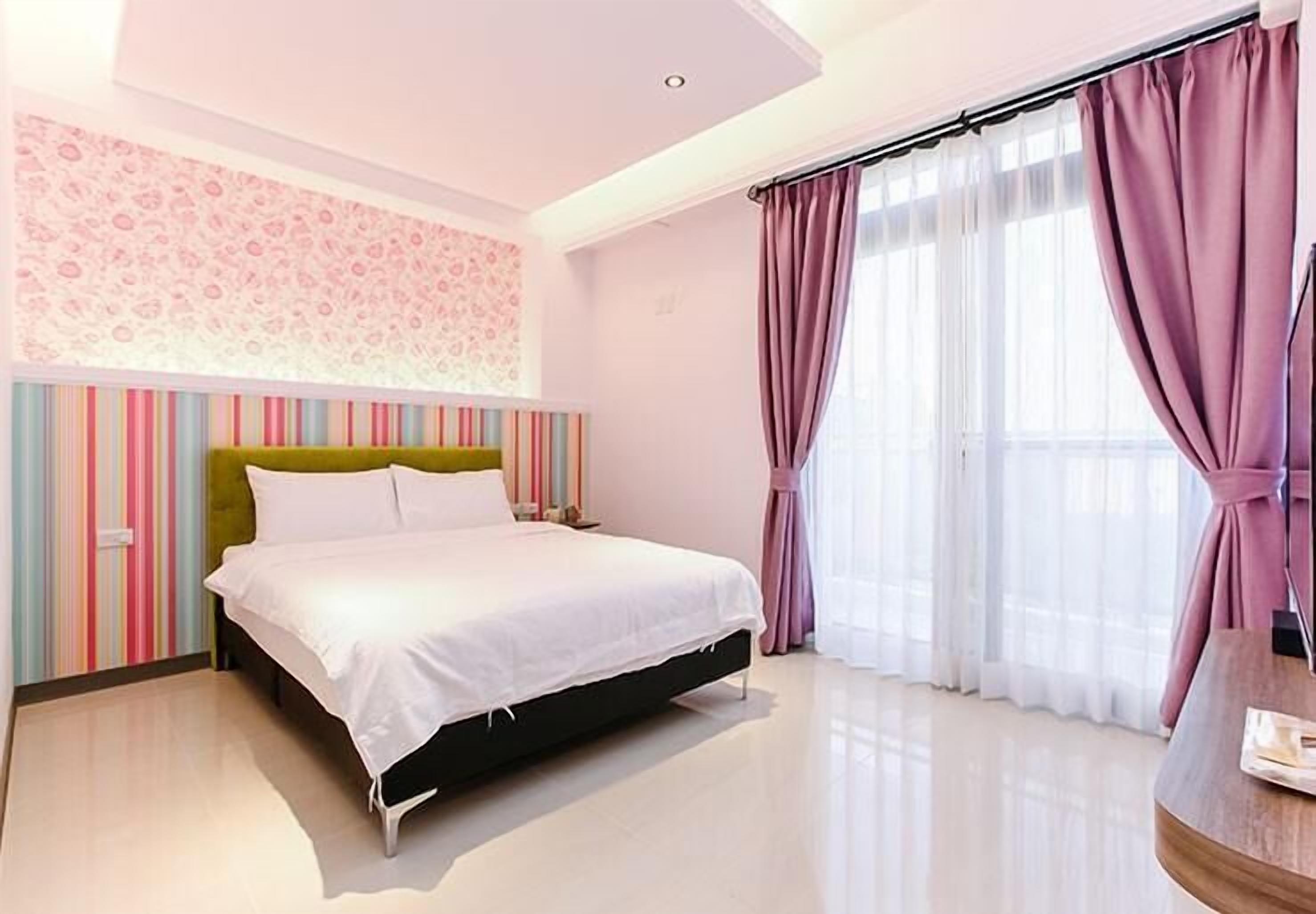 A modern bedroom with a bed, a wall with a floral pattern, and a window with curtains.