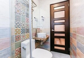 Un baño con ducha, inodoro, lavamanos y una puerta con panel de vidrio esmerilado.