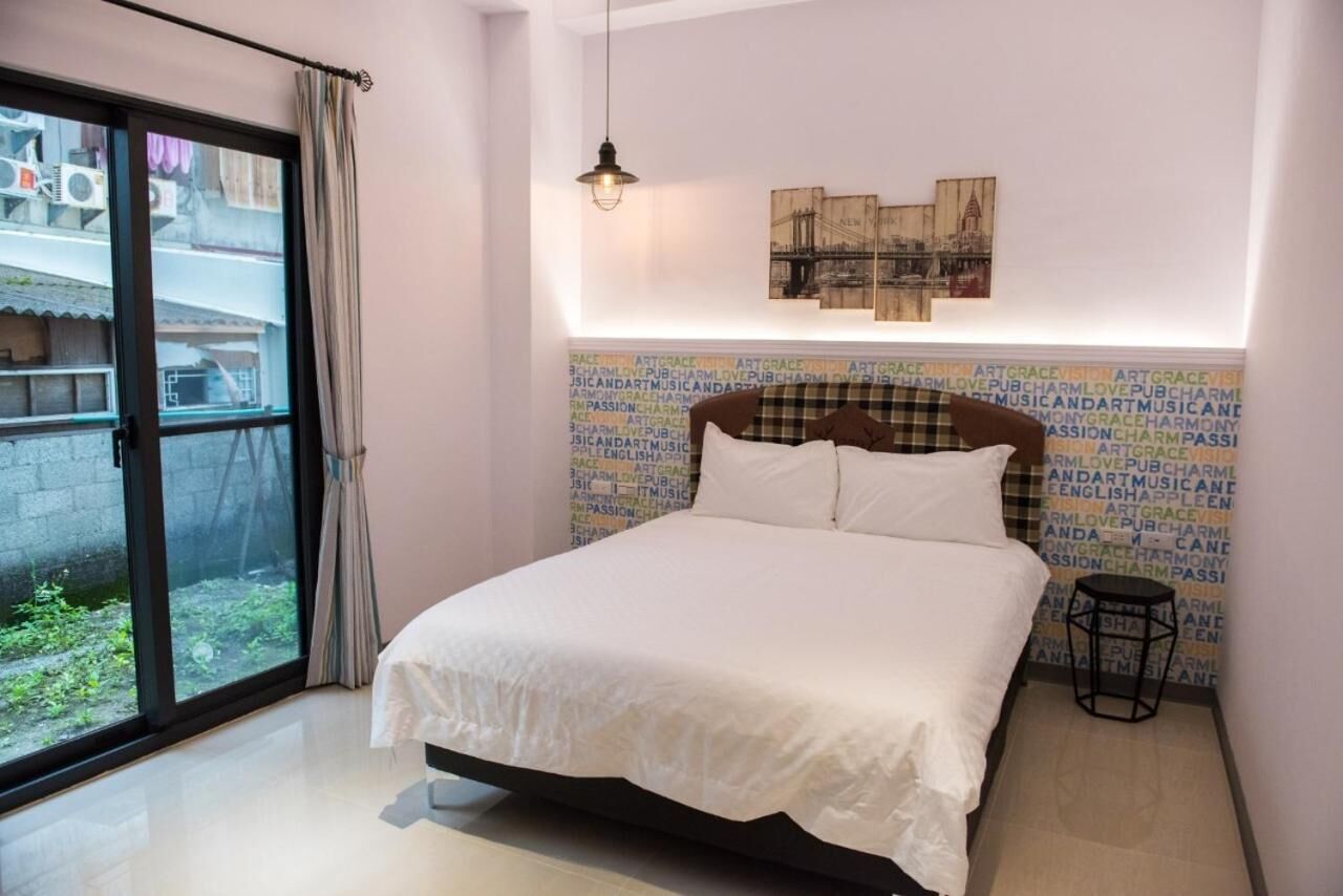 A bedroom with a bed, a window with curtains, a wall with text, and a hanging light fixture.
