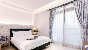 Un dormitorio moderno con una cama grande, una mesita de noche, una silla y una ventana con cortinas.