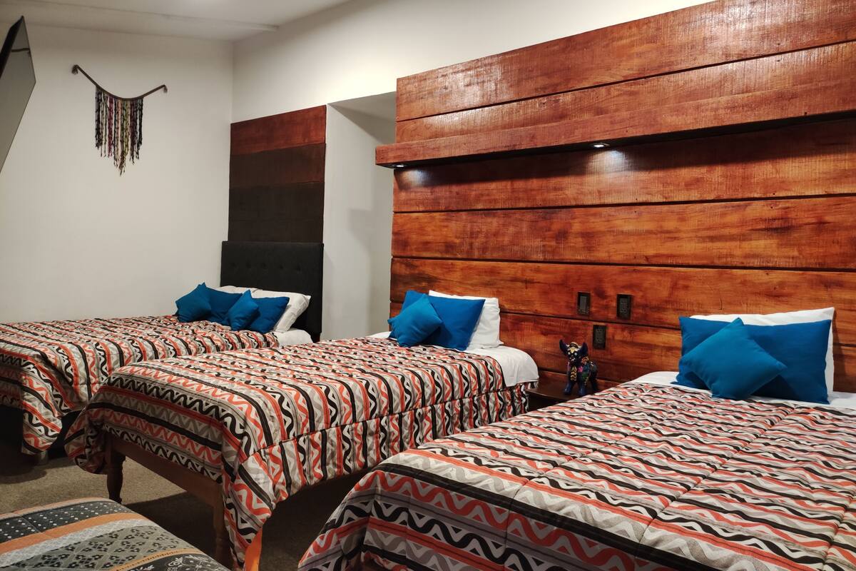 Ein Hotelzimmer mit zwei Betten, jeweils mit gemusterten Bettbezügen und blauen Kissen. Das Zimmer verfügt über Holz-Kopfteile und eine dekorative Wandgestalt.
