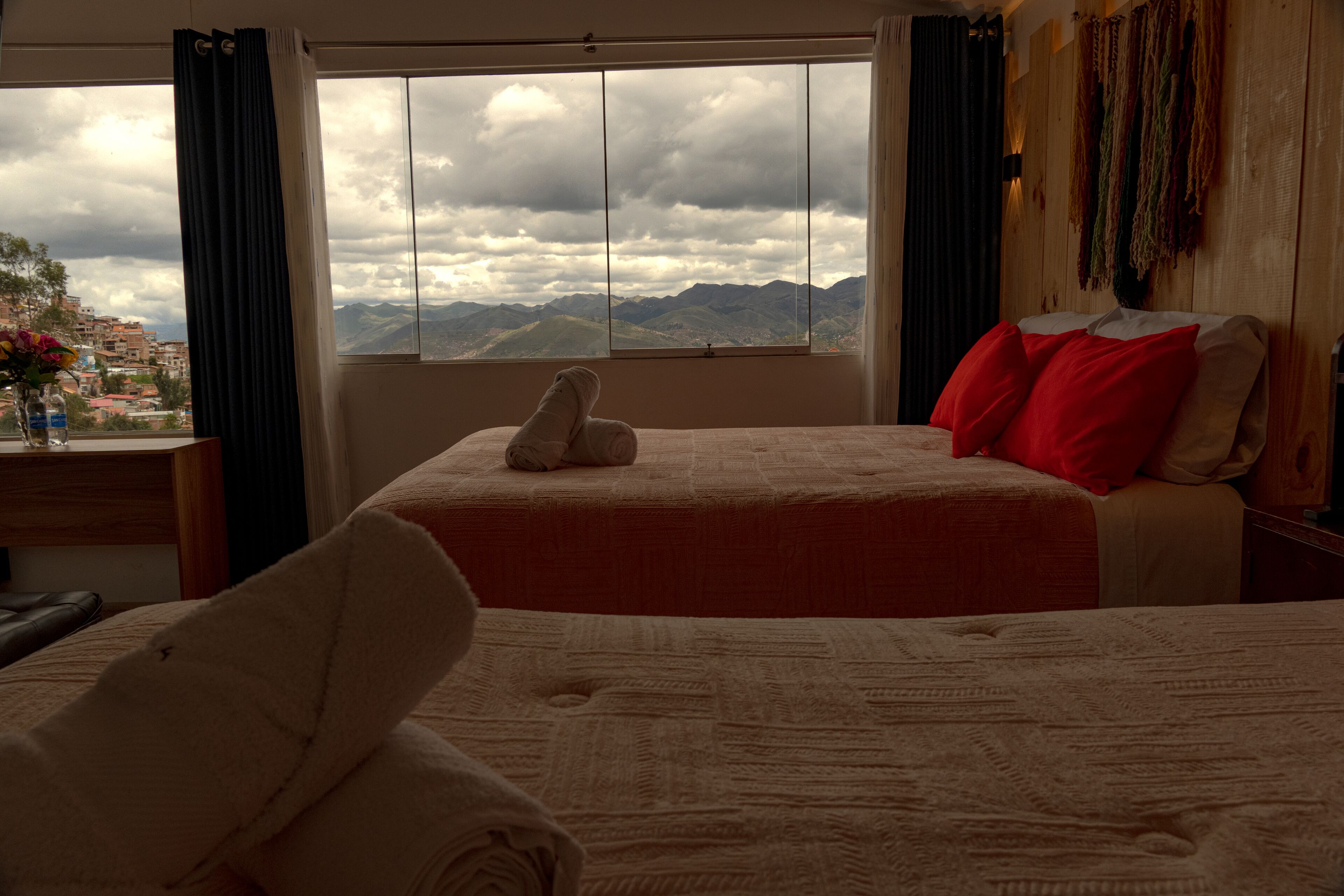 Habitación de hotel con un ventanal grande que ofrece vistas a la montaña, una cama con ropa de cama roja y blanca, y un cabecero de madera.
