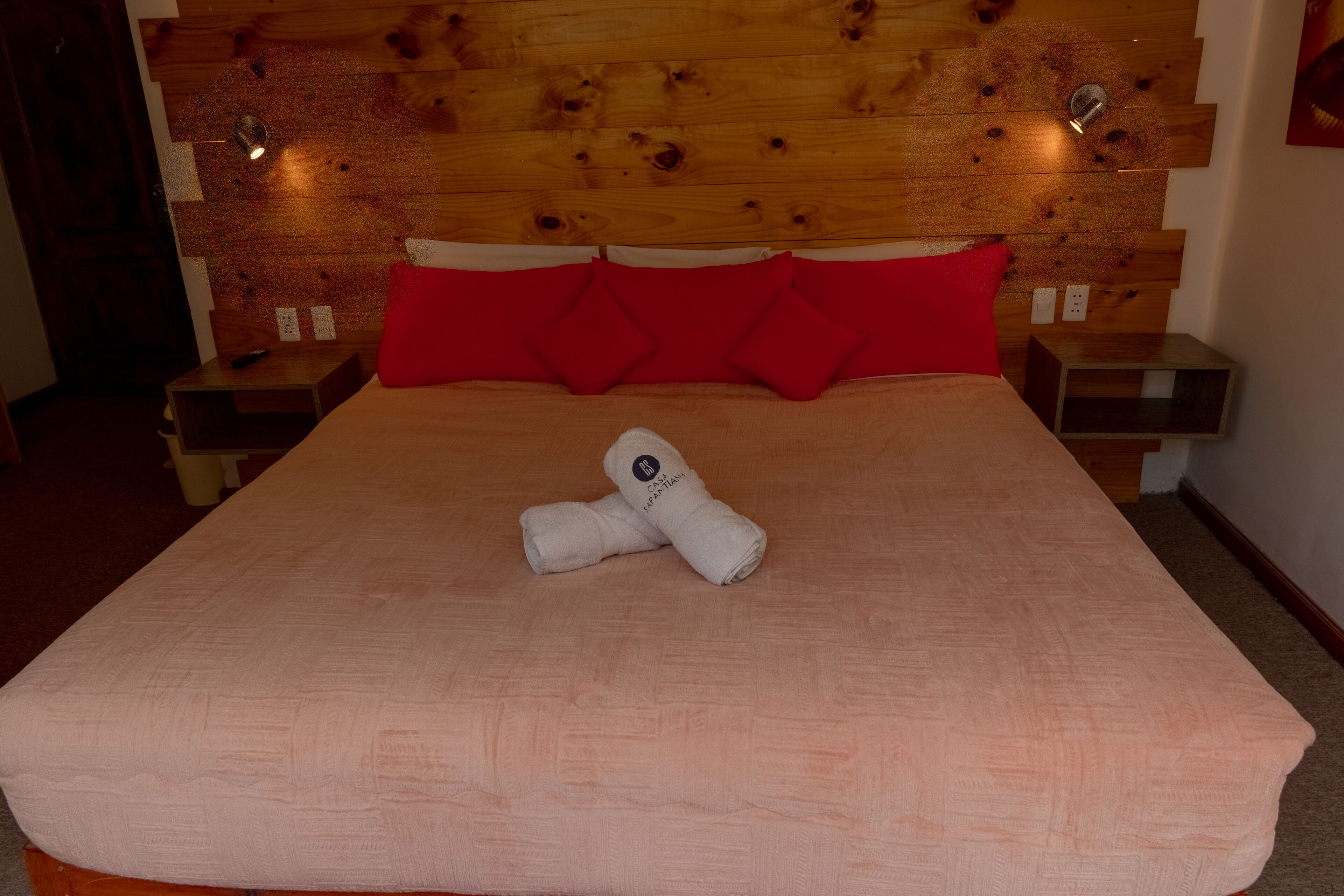 Una cama bien hecha con cabecera de madera, almohadas rojas y una toalla doblada sobre la cama.