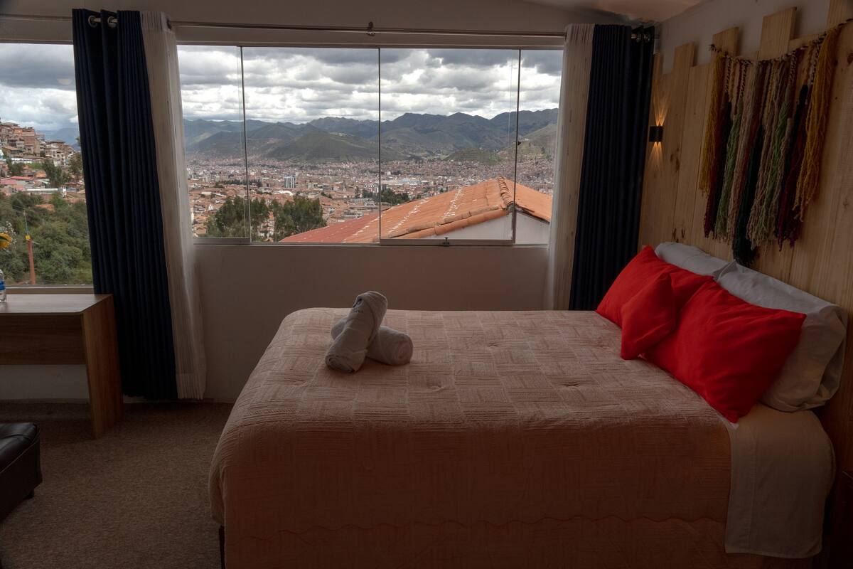 Ein Hotelzimmer mit Bett, Blick auf Stadt und Berge sowie einem Holzkopfende.