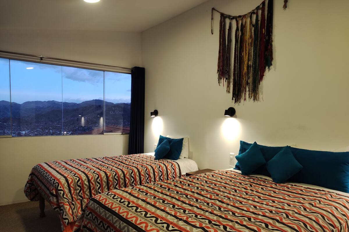 Ein Hotelzimmer mit zwei Betten, einem großen Fenster und Blick auf die Stadt sowie einer Wand mit einem Traumfänger.