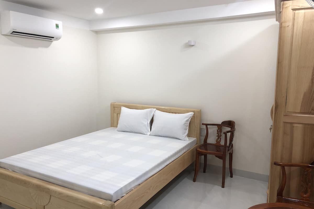 Ein Schlafzimmer mit einem hölzernen Bett, weißer Bettwäsche, einem Holzstuhl und einem Kleiderschrank.