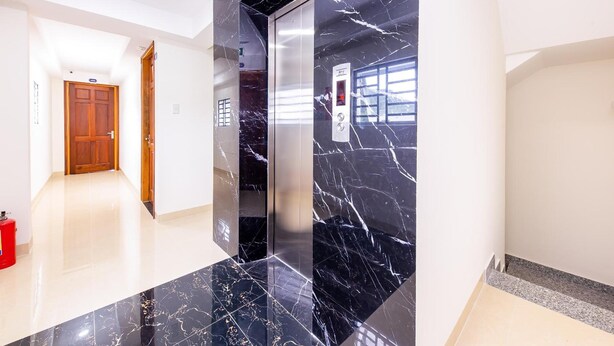 A modern elevator with marble walls and a polished floor, leading to a wooden door. - OYO 572 The Wanda Hotel (Nam Nha Trang)