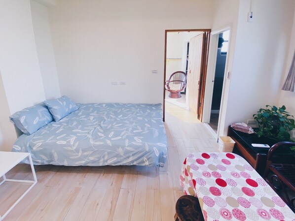 A small, bright room with a bed, a desk, and a chair. There is a door leading to another room. - Tree House Café & Homestay (Tongluo)