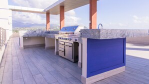 Une cuisine extérieure dotée d’un barbecue et d’un four intégrés, située sous un patio couvert offrant une vue sur la ville et les montagnes.