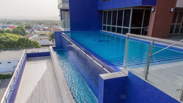 Une piscine sur le toit, avec une eau d’un bleu cristallin, entourée d’un bâtiment moderne doté de grandes fenêtres.