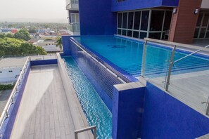 A rooftop swimming pool with clear blue water, surrounded by a modern building with large windows.