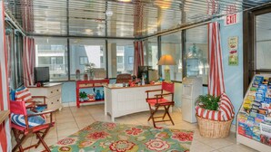 A room with a curved desk, two chairs, a lamp, a basket with a plant, and a wall with an exit sign. - Sea Pointe 906-Oceanfront 1BR-Indoor Pool-Hot Tub (NORTH MYRTLE BEACH)