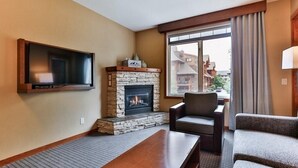 A hotel room with a stone fireplace, a flat-screen TV mounted on the wall, a sofa, and a window with curtains.