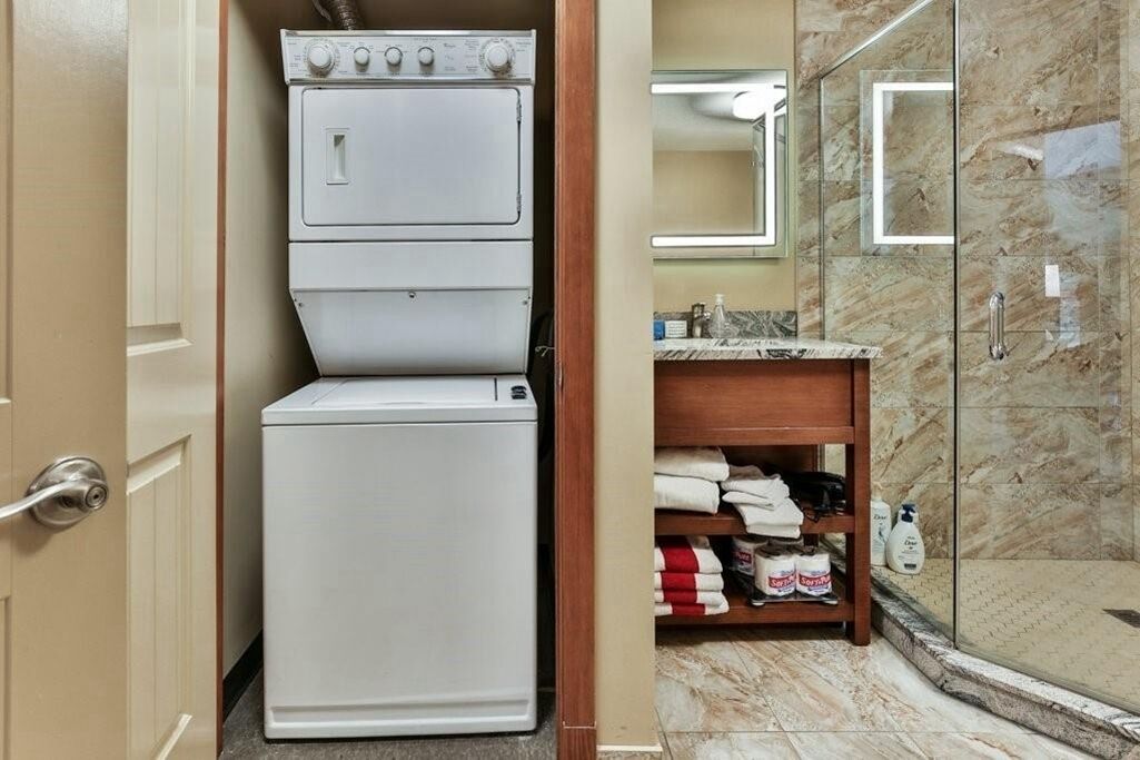 Une salle de bain compacte dotée d’un lave-linge et d’un sèche-linge intégrés, d’une douche en verre et d’un sol carrelé en marbre.