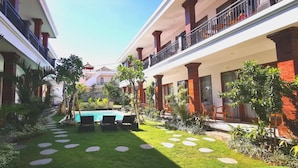 A courtyard with a swimming pool, palm trees, and a garden path. - Santi HomeStay (Canggu)