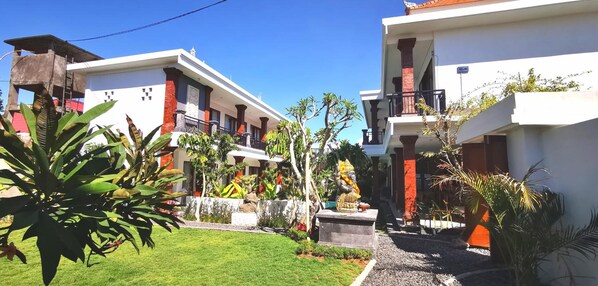 A two-story hotel with a garden courtyard, featuring a statue and tropical plants.