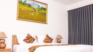 A hotel room with a bed, two bedside lamps, a nightstand, a large painting of a field, and a window with curtains. - Santi HomeStay (Canggu)