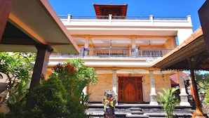 A two-story building with a balcony, a wooden door, and a statue in front. - Santi HomeStay (Canggu)
