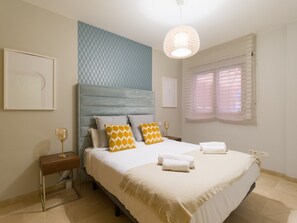 A bedroom with a bed, bedside tables, a hanging light fixture, and a window with blinds.