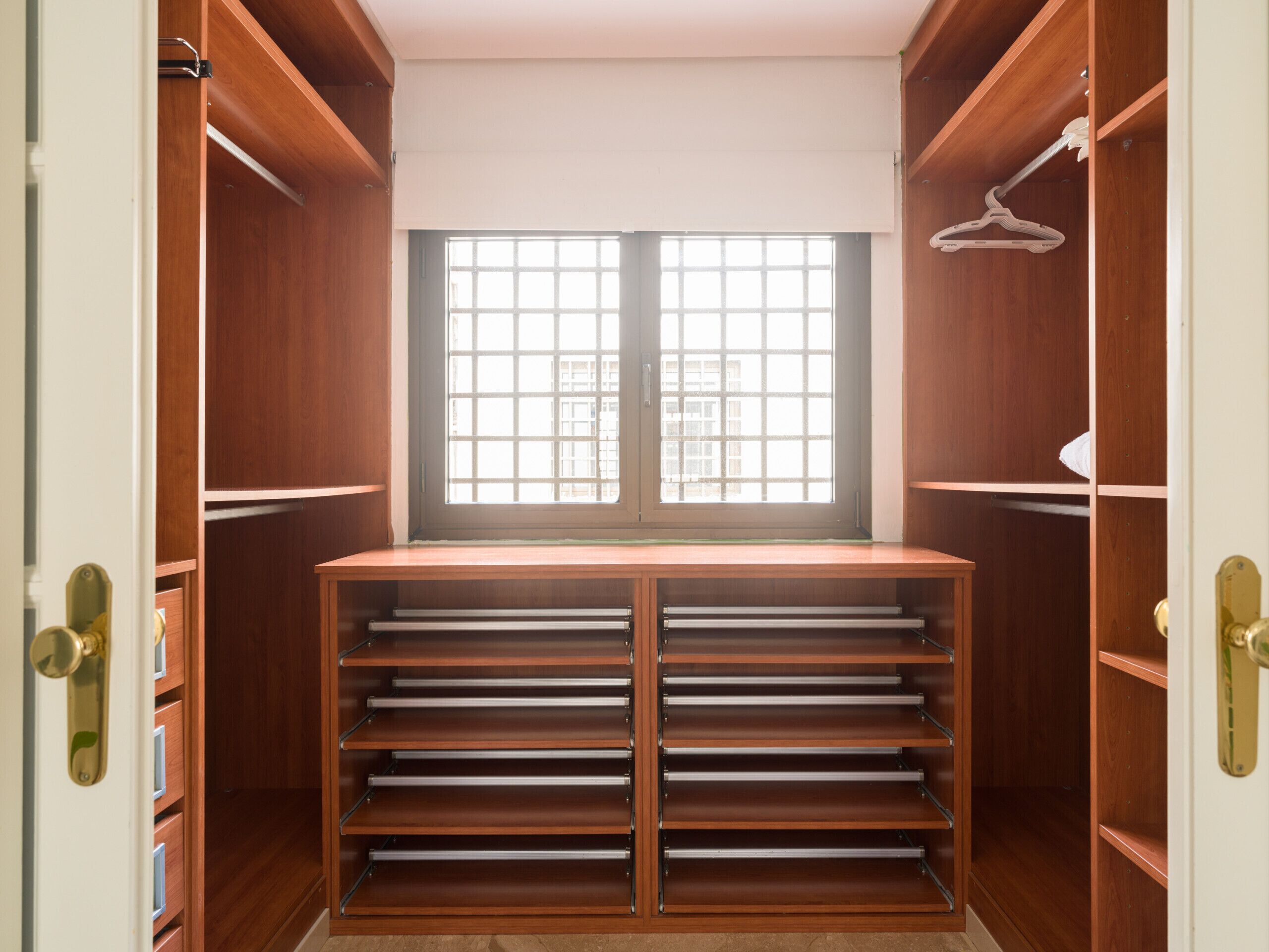 A walk-in closet with a large window, multiple shelves, and a hanging rod.