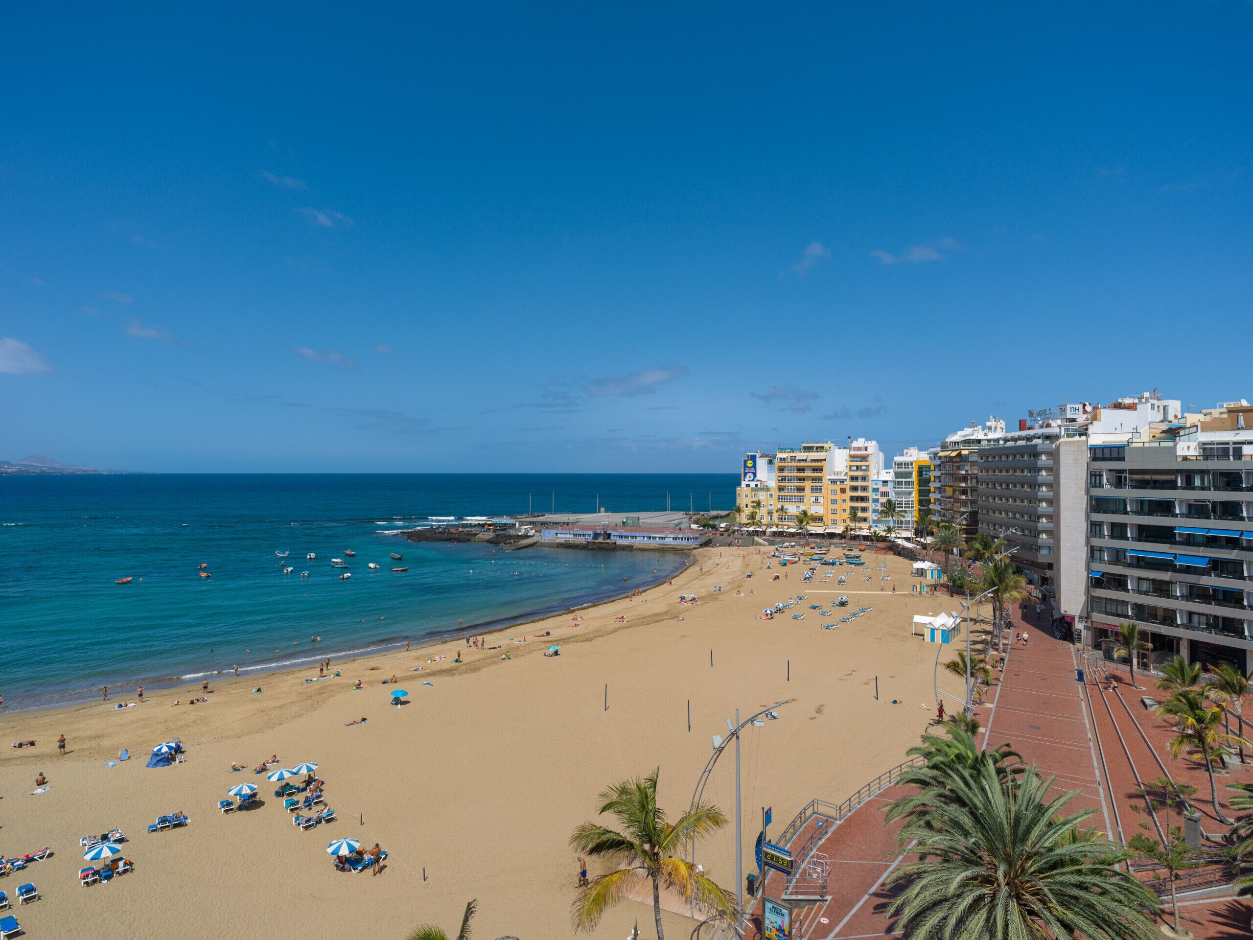 Uma praia com águas azuis cristalinas, faixa de areia e uma fileira de edifícios com varandas com vista para a praia.