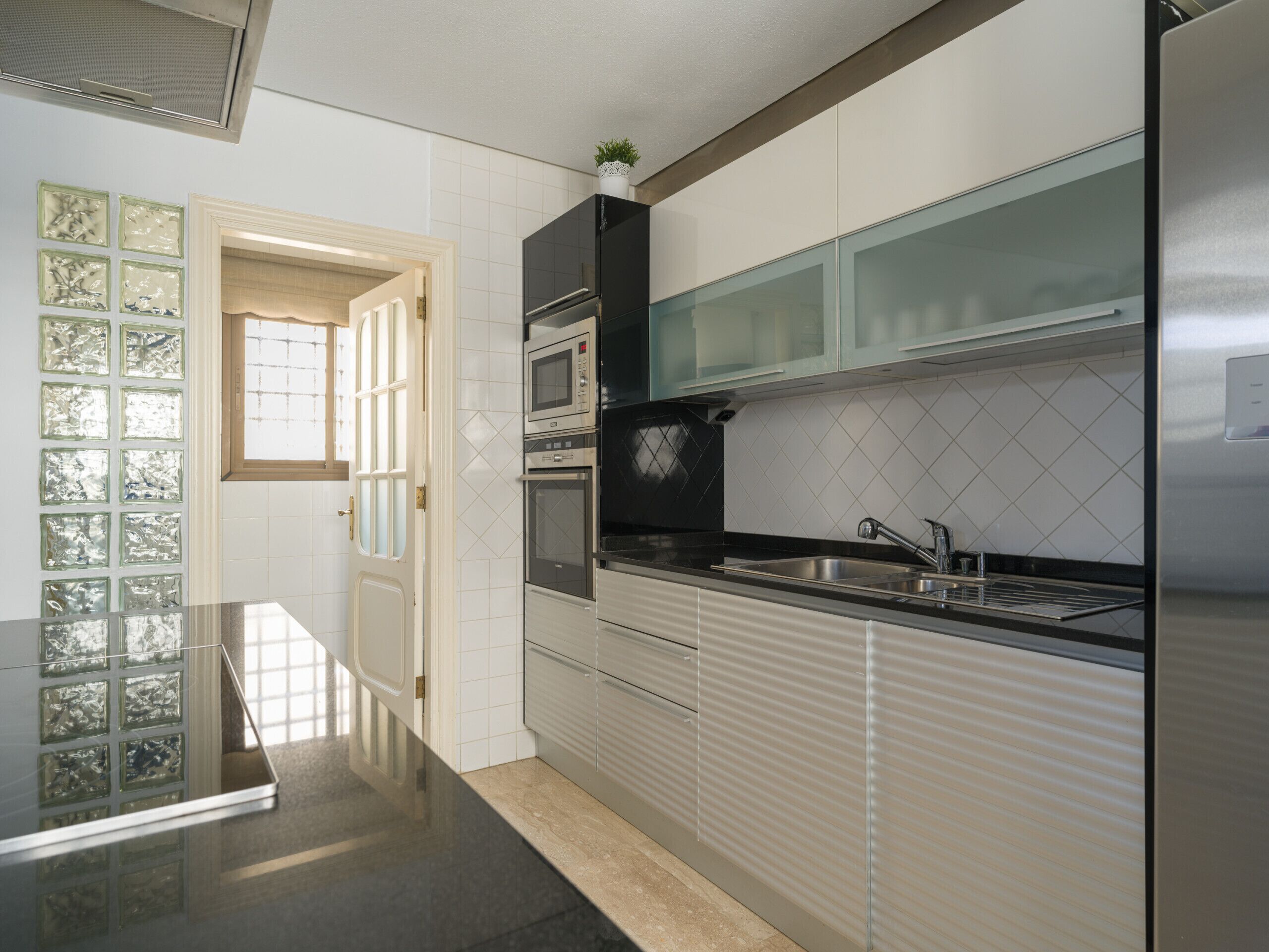A modern kitchen with stainless steel appliances, a black countertop, and a window with frosted glass panels.