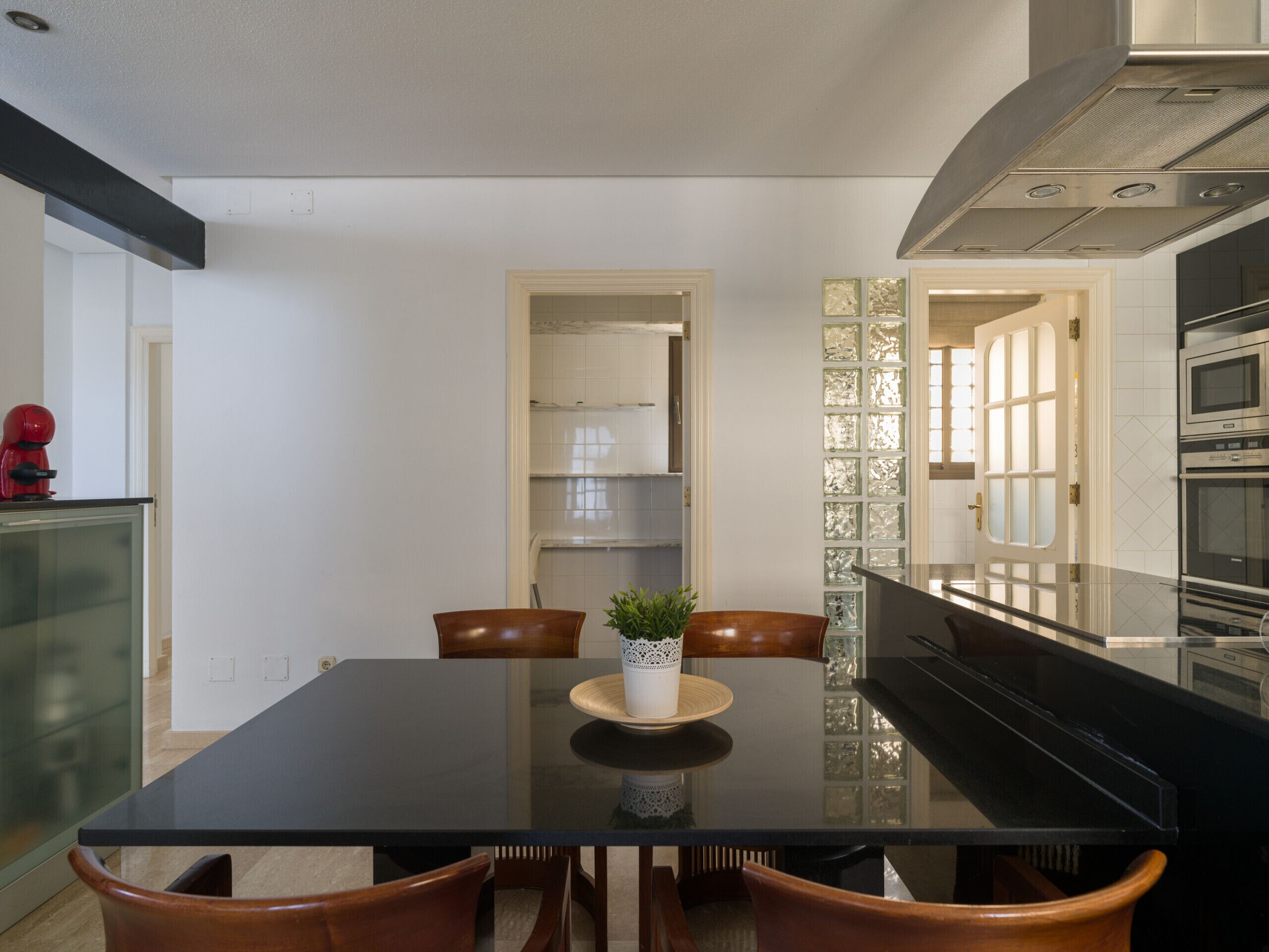 A modern kitchen with a black countertop, stainless steel appliances, and a glass dining table.