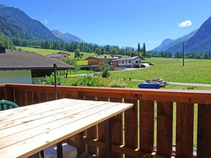A wooden deck with a table, overlooking a rural landscape with houses and mountains. - Apartment Anna by Interhome (Umhausen)