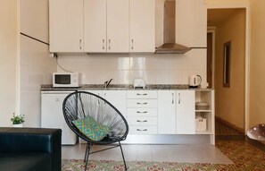A compact kitchen with white cabinets, a microwave, and a black chair with a patterned cushion.