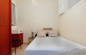 A small hotel room with a bed, a nightstand, a chair, a window, and a door.