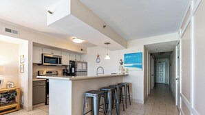 Una cocina moderna con una isla central, taburetes de bar, electrodomésticos de acero inoxidable y vistas al pasillo que lleva a una puerta.