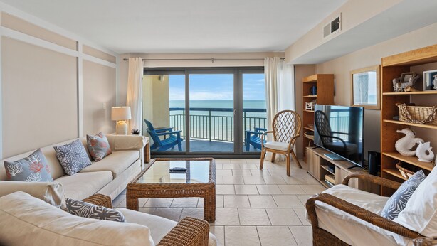 Amplia sala de estar con televisor grande, asientos cómodos y un balcón con vista al mar.