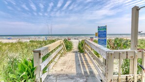 Un paseo marítimo de madera que conduce a una playa, con un cartel que indica 6144 Walkway.