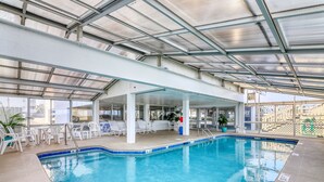 Una piscina interior con techo cubierto, sillas de descanso blancas y vista despejada al exterior.