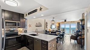 Una cocina moderna con armarios oscuros, una isla grande y un comedor con vista al océano.