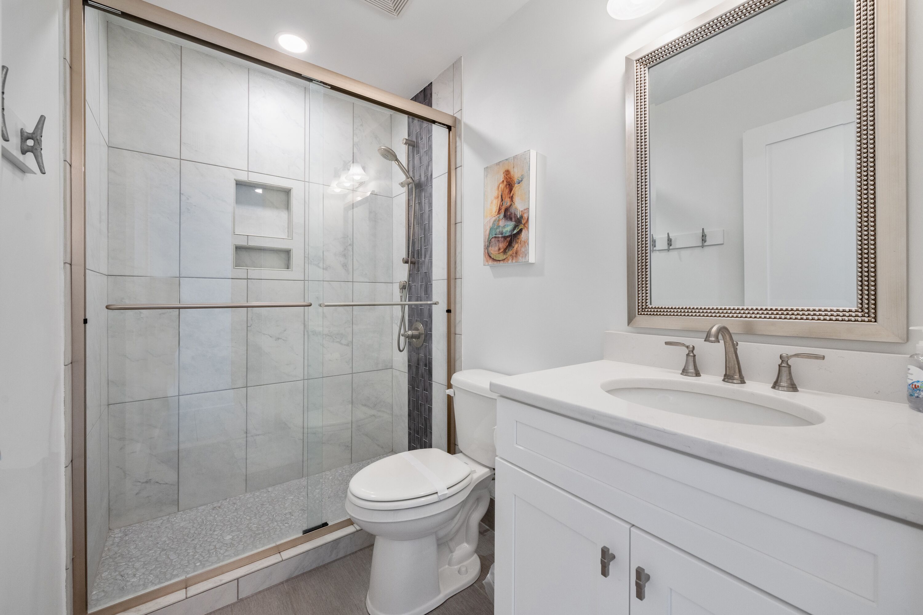 A modern bathroom with a glass-enclosed shower, a white toilet, a large mirror, and a white vanity with a sink.